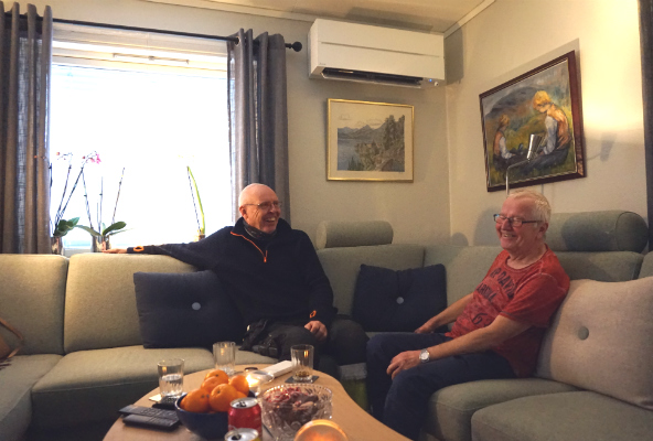 Per-Arne og Thorleif sitter i en sofa. Varmepumpe på veggen. Foto. 