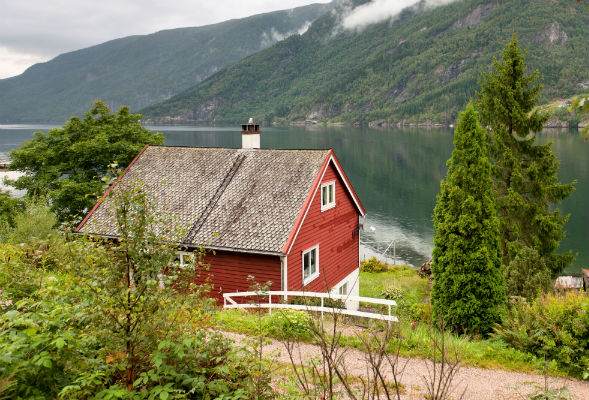 Et rødt hus som ligger ved vannet i en fjord. Foto. 