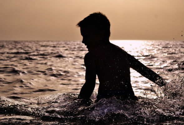Barn som leker i vannet, i solnedgang. Foto. 