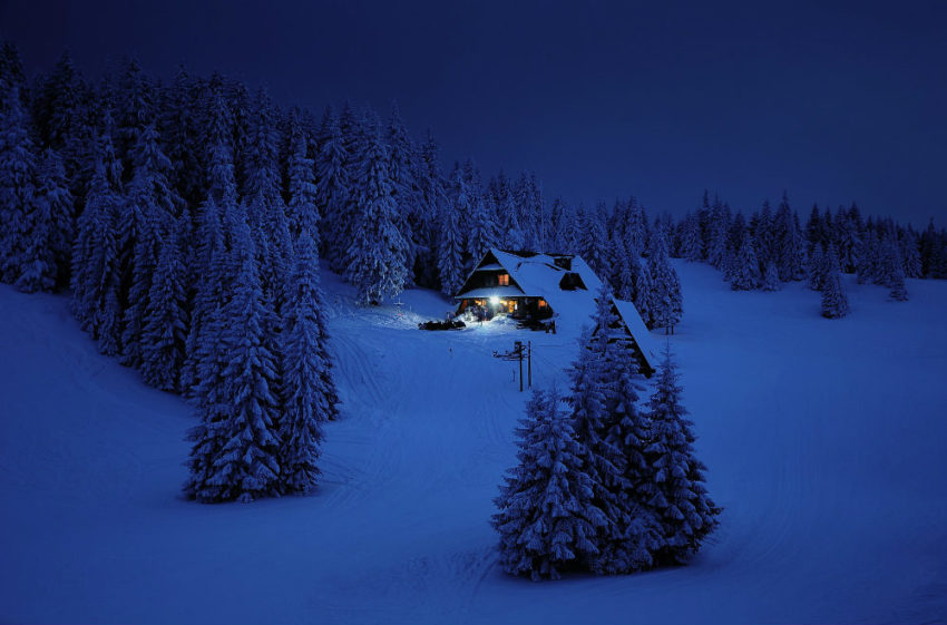 Hytte i mørkt snølandskap. Foto.