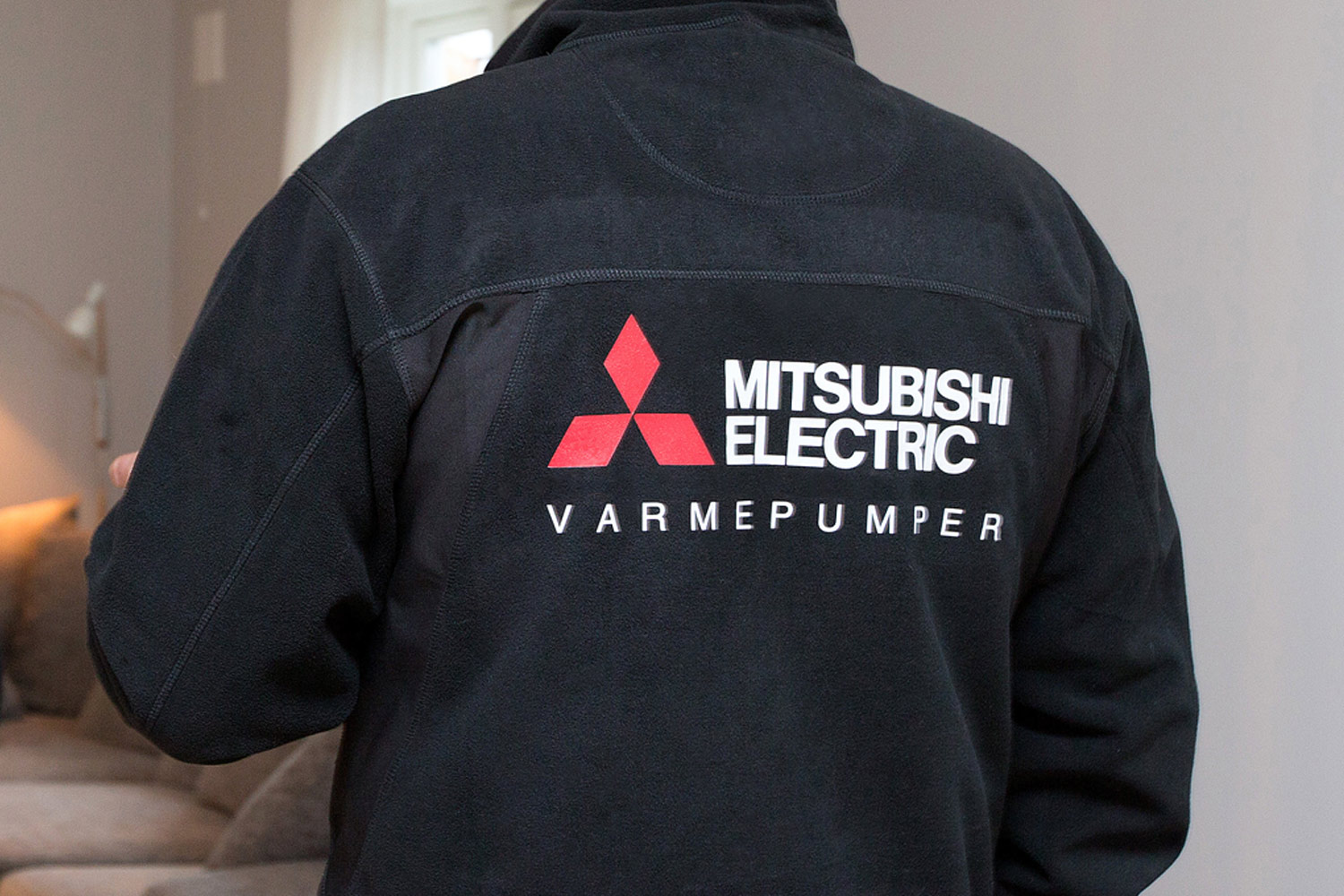 Mitsubishi Electric på ryggen til montør. Foto.