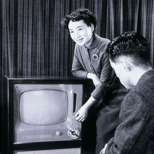 Dame skrur på knappen på en gammeldags TV. Svart/hvitt- foto.